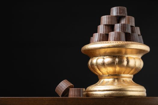 Stack of Fine Chocolates On Golden Pillar Dish With Dark Background.