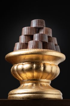 Stack of Fine Chocolates On Golden Pillar Dish With Dark Background.