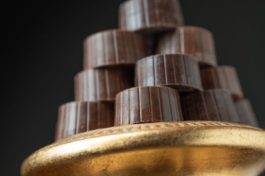 Stack of Fine Chocolates On Golden Pillar Dish With Dark Background.