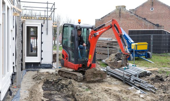 Small crane is leveling ground at a building site of a dutch house