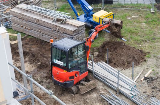 Small crane is leveling ground at a building site of a dutch house