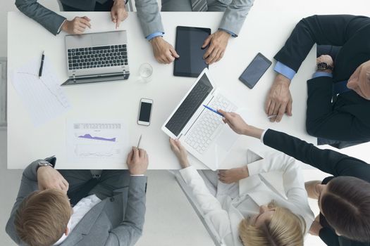 Business people brainstorming at office desk, analyzing financial reports and working with laptops and tablets