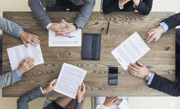 Top view of confident business men in suits sitting at wooden table and discussing new contract terms before signing it