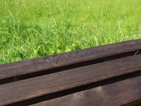 I Love You with a Heart Carved into a Wooden Bench with grass background