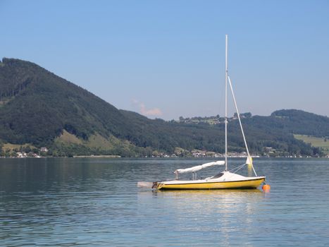 Yellow Sailboat on Blue Lake with Large Mountain Background in Summer