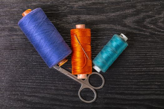 colored threads and scissors on a black wooden background