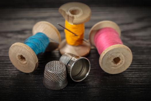 Thread and thimble on a black wooden background