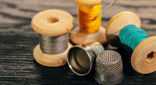 Thread and thimble on a black wooden background