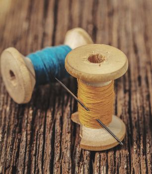 colored threads and needle on wooden background