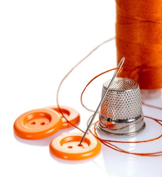 Needle with orange thread and buttons on a white background