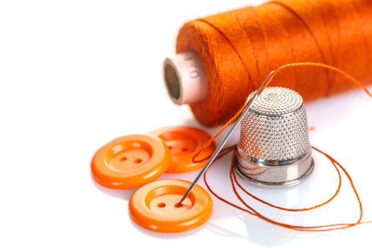 Needle with orange thread and buttons on a white background