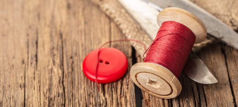 red thread with buttons and scissors, wooden background