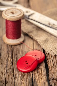 red thread with buttons and scissors, wooden background