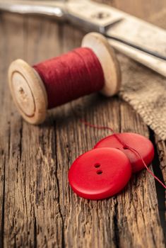 red thread with buttons and scissors, wooden background