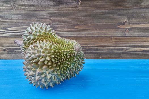 Durio zibethinus or Durian ripe with spikes on blue sea and brown jane wooden texture background with copy space. Mon thong is King of fruits from Thailand.