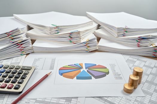 Pencil and pie chart of sale report monthly with step pile of gold coins and calculator have blur overload paperwork on wooden table with white background. Business and finance concept successful.