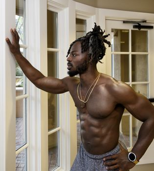 Handsome muscular shirtless African American man looking through the window.