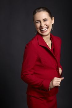 Studio shot of laughing young woman in red skirt suit on black background.