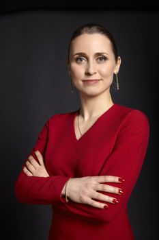 Business portrait of young confidence woman in red dress and arms crossed on black background.