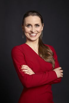 Studio portrait of young satisfied woman with long hair, white smile, green eyes and crossed arms on black background.