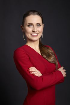 Portrait of young woman with long blonde hair, white smile, green eyes and crossed arms on black background.