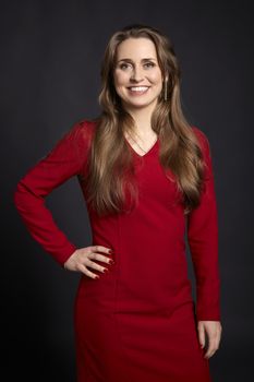 Studio portrait of young cheerful woman with long hair, white smile, green eyes and hand on hip on black background.