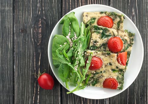Frittata with spinach and tomatoes. Top view on a wooden table.