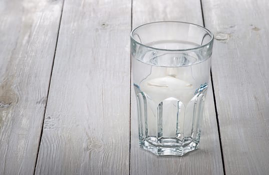 A glass of water on a white wooden table. Blurred background.
