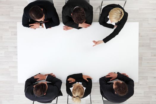 Business people sitting around empty table, business woman pointing to blank copy space in the middle