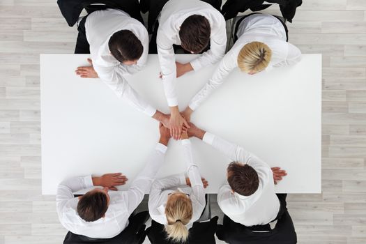 Business people team stacking hands sitting around white conference table in office