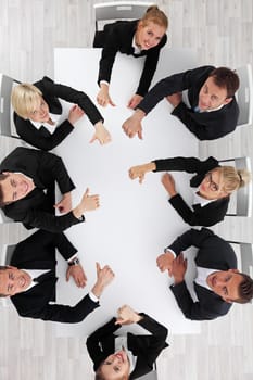 Business people showing thumbs up sitting around white conference table in office