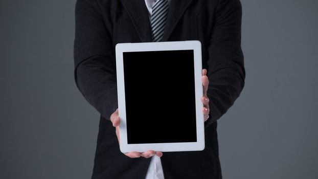 Businessman holding tablet in black suit on gray background