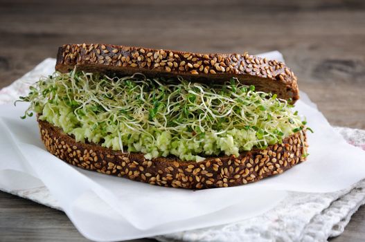 Sandwich of tender, juicy germinated alfalfa and avocado sprouts on slices of rye bread with cereals. This is a great idea for those who watch their health.