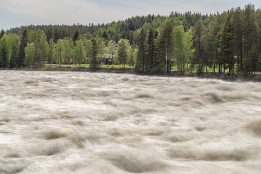 The Rapids at Renforsen in Vindeln, Sweden with a partly cloudy sky and red houses.