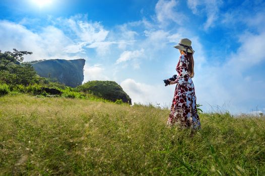 Woman standing on meadow and holding camera at Phu Chi Fa mountains in Chiangrai, Thailand. Travel concept.
