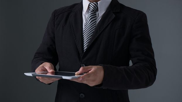 Businessman holding tablet in black suit on gray background