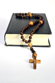 black book of the Bible with wooden rosary on white background