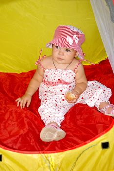 girl in a hat sitting in the red and yellow tent child