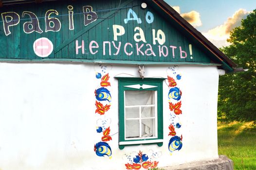 white facade of the Ukrainian hut with a painting around the windows and inscription slaves in heaven are not allowed