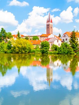 Tower of Church of the Holy Spirit in Telc on sunny summer day reflected in the water, Czech Republic.