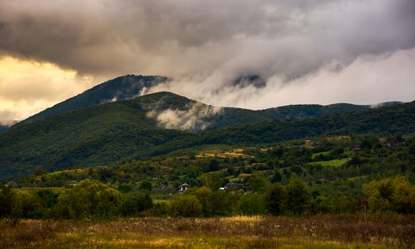 rising clouds in mountainous countryside at menacing sunrise. village at the foot of the mountain. rainy weather