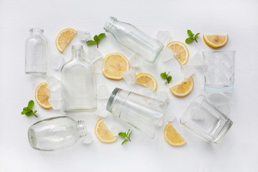 Glasses and bottle for drinks with lemon slices, mint and ice on white. Healthy vitamin drink concept.