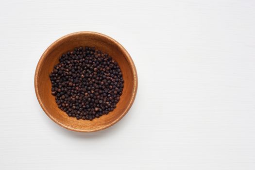 Black peppercorn in wooden bowl isolated on white background.