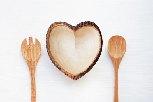 Wooden dish heart shape with spoon and fork on white background.