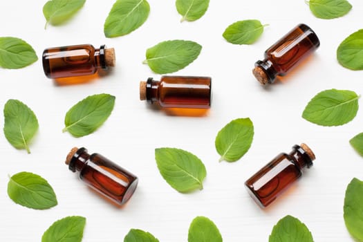 Mint Essential Oil in a Glass Bottle with leaves on white background.