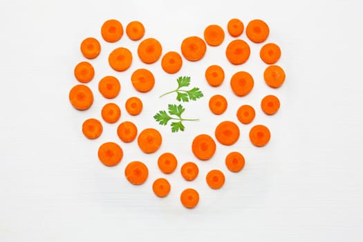 Chopped carrot slices heart shape and parsley leaves  isolated on white background.