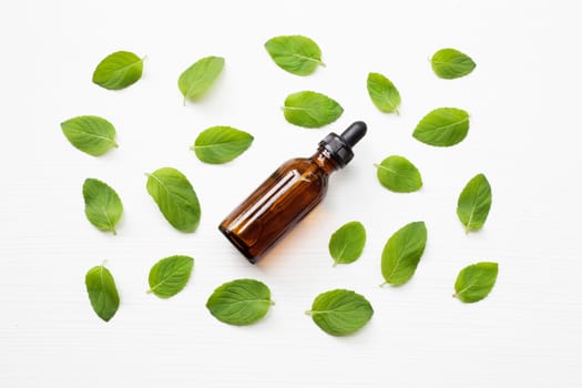 Mint Essential Oil in a Glass Bottle with leaves on white background.