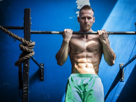 Blond, attractive young man hanging from gym equipment, looking at camera