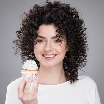 Happy cute lovely curly young woman with curly hair holding cupcake and smiling