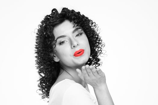 Pretty young woman with curly hair sending air kiss isolated over white background